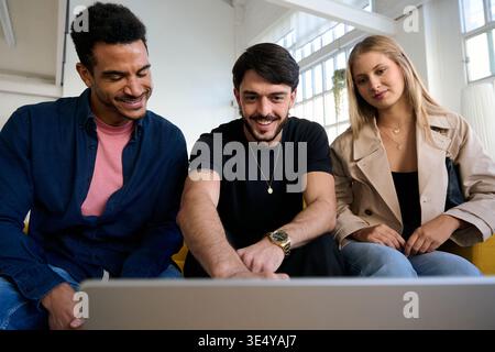 Diverse smiling young friends collaborating discussing project looking at laptop Stock Photo