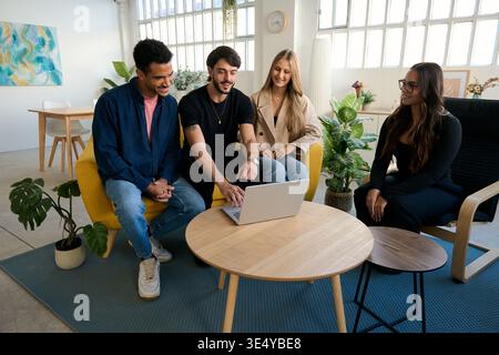 Diverse colleagues collaborating on laptop in modern office lounge Stock Photo