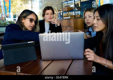 Diverse women collaborating on laptop in cafe Stock Photo