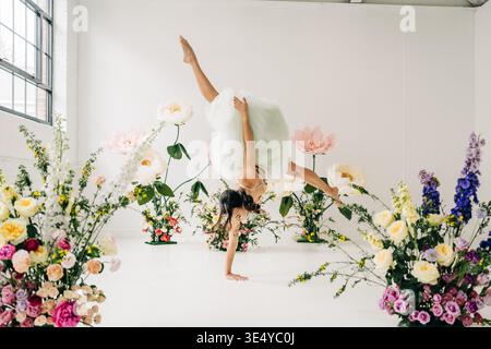 Woman performing handstand in blooming floral studio Stock Photo