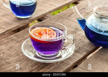 Blue and purple tea, an infusion of butterfly pea flowers, with a citrus, two cups and a teapot on a wooden table outdoors Stock Photo