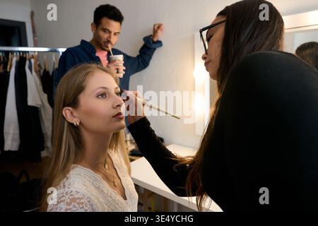Makeup artist applying cosmetics backstage to young model Stock Photo