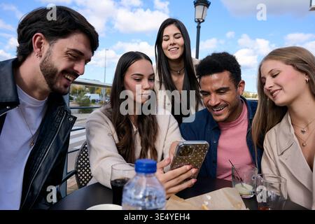 Diverse friends enjoying phone content at outdoor cafe Stock Photo