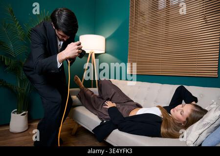 Man covertly photographing woman sleeping on sofa at home Stock Photo