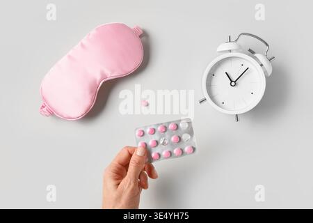 Pink sleeping mask, watch, alarm and pink vitamins capsules on gray background. Concept of sleep, health care, daily routine and circadian rhythms. Stock Photo