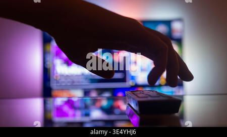 TV with streaming with a remote control near the wall in the room. news and series online. Watching videos on TV. Hand takes TV remote control Stock Photo