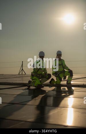 Male and female engineers inspecting solar panel installation points on a rooftop under sunlight, representing clean energy and sustainable development || Model released Stock Photo