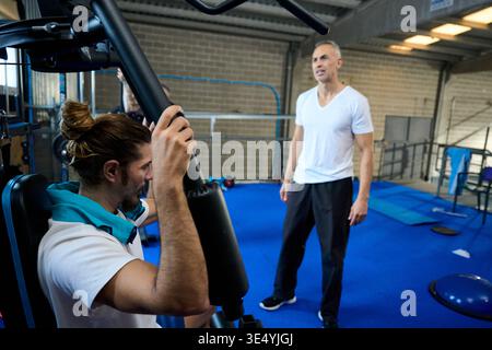 Personal trainer guiding man doing strength workout Stock Photo