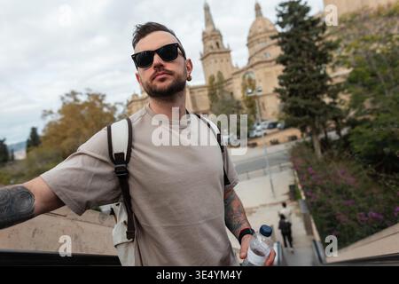 Cool hipster traveler man with trendy sunglasses in beige t-shirt with backpack traveling in Barcelona, ​​Spain Stock Photo