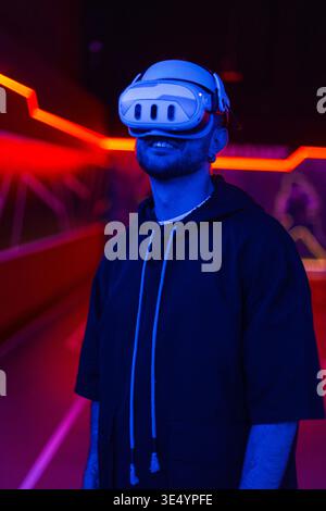 Happy handsome smiling man with VR glasses using online virtual interface in room with neon lights Stock Photo