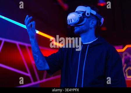 Bearded young man in virtual reality glasses in the studio with blue and pink light. Stock Photo