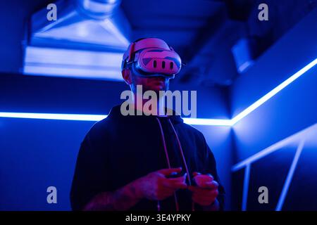 Man with VR glasses playing games in a neon room. Virtual world online Stock Photo