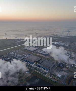 Aerial view of large data center facilities with cooling systems emitting steam, powered by wind turbines, at sunset, supporting ai technology Stock Photo