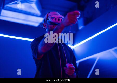 Cool man with VR glasses plays games with joysticks in neon light. Metaverse, virtual reality glasses and a man with vr control futuristic gaming, cyb Stock Photo