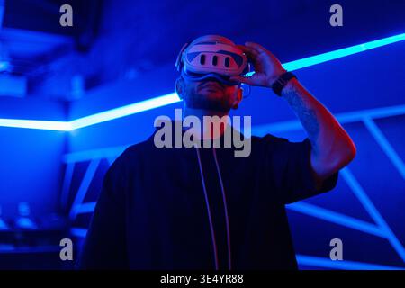 Cyber ​​man with VR glasses uses headset in virtual world in dark room with neon light Stock Photo