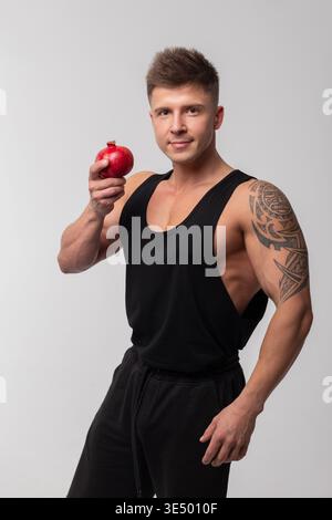 Muscular handsome healthy man in black t-shirt holding pomegranate. Diet and vitamins Stock Photo
