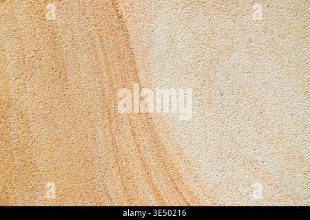 Close-up texture of rough-cut sandstone wall surface showing natural tonal variation from pale cream to warm amber, with a darker diagonal streak. Stock Photo