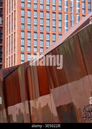 Weathered Corten steel panels with rust patina in the foreground, red brick high-rise building visible behind, urban setting. Stock Photo