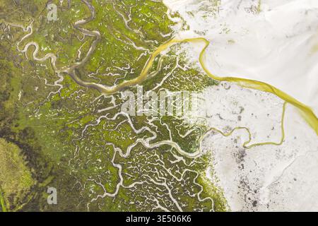 Aerial view of winding water channels through green salt marshes and white sand flats in Goulven, Brittany, France. Stock Photo