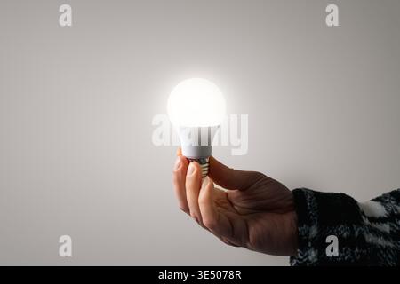 Hand Holding LED Light Bulb on Neutral Background Concept of Idea Energy and Innovation. High quality photo Stock Photo