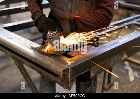 Worker hands operating angle grinder on welded metal construction creating shower of sparks in outdoor workshop Stock Photo