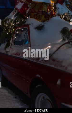 Red vintage car with snow, lights, Christmas tree branches and gifts at night. Christmas card Stock Photo
