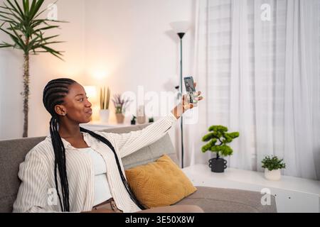 Young Black woman smiling taking selfie with smartphone at home Stock Photo