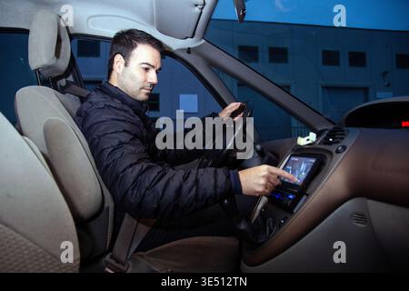 Young man driving vehicle on road, using modern in car touchscreen technology, interacting with digital display for navigation or infotainment, focusi Stock Photo