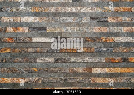 Texture of a modern stacked stone veneer wall featuring horizontal layers of mixed natural slate and marble tiles as background Stock Photo