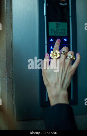 Hand of a woman with multiple rings pressing a button on a modern intercom system, illuminated display showing options in a contemporary building Stock Photo