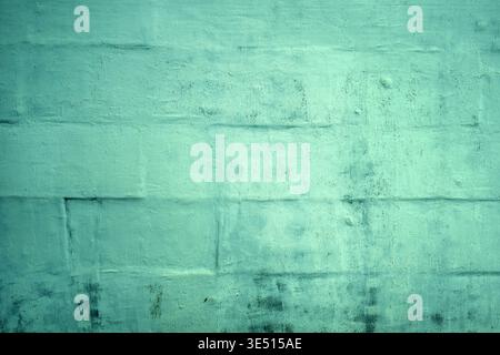 Texture of a rough concrete block wall coated in soft turquoise-green paint, showing subtle brush strokes, micro-cracks, faint peeling spots as backgr Stock Photo
