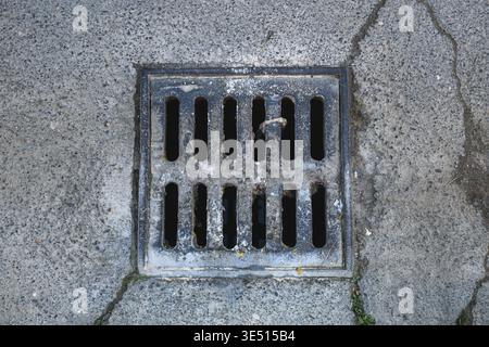 Rusty metal drainage grate embedded in cracked concrete sidewalk, top view Stock Photo