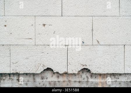 Old worn styrofoam slabs fixed on unfinished building wall as thermal insulation. Rough construction facade with exposed insulation boards and weather Stock Photo