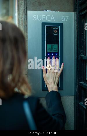 Woman with multiple rings pressing intercom button at building entrance, displaying the name 'SUECA' and number '67' on the panel Stock Photo