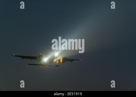 Airplane approaching landing with bright landing lights illuminated against a dark sky, showcasing the aircraft's silhouette and runway lights in the Stock Photo