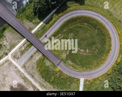 Aerial view of a winding bike path snakes through vibrant green fields, contrasting with the adjacent river and crossing paths, Nederstichtselaan, Alm Stock Photo
