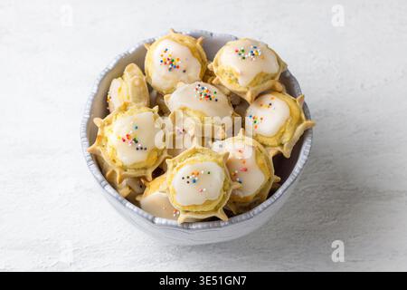 Traditional Sardinian ricotta cheese cookies with sugar glaze and sprinkles in ceramic bowl on white background Stock Photo