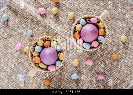 Cups with colored egg and colored chocolate eggs on a creamy background, top view Stock Photo