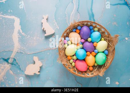 Colorful colored easter eggs in a basket and decorative easter bunnies on a turqoise background, top view, copy space Stock Photo