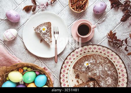 A piece of nut cake on a plate and colored easter eggs on the easter table. Low carb, keto, diet food. Top view. Stock Photo