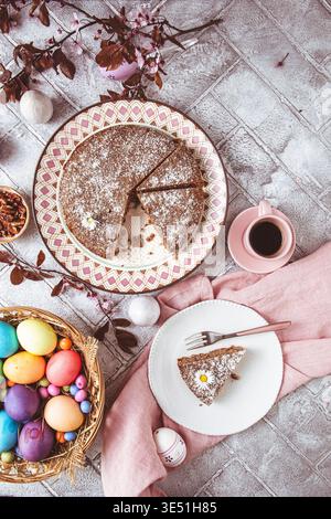 A piece of nut cake on a plate and colored easter eggs on the easter table. Low carb, keto, diet food. Top view. Stock Photo