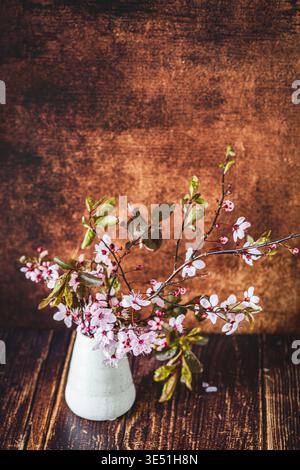 Vase with branches of blood plum on a wooden background. Red-leaved cultivars of the cherry plum (Prunus cerasifera) are called blood plums. Vertical Stock Photo