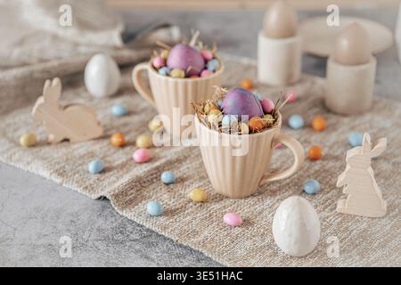 Cups with colored egg and colored chocolate eggs on a creamy background, top view Stock Photo