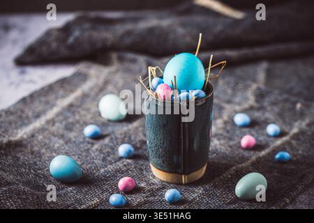 Dark blue stoneware cup with blue colored egg and colored chocolate eggs on a dark background. Stock Photo
