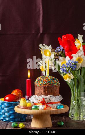 Easter composition with kulich, painted eggs, bouquet of daffodils and tulips, and candles Stock Photo