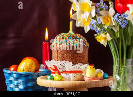 Easter composition with kulich, painted eggs, bouquet of daffodils and tulips, and candles Stock Photo