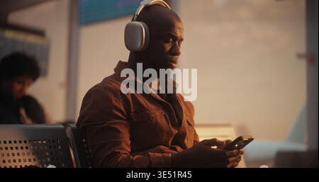 While Waiting For Flight, Focused African American Passenger Uses Mobile Device to Send Messages, Coordinating Business Details or Checking in With Contact. Efficiency of Modern Digital Traveler. Stock Photo