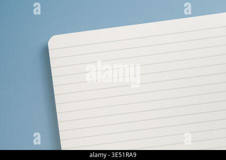 Blank spiral notebook lies open on a blue background. Open pages are lined and ready for writing or drawing. Top view Stock Photo