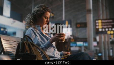 Woman Sits in International Airport Terminal, Using Smartphone Scan QR Code on Boarding Pass. Female Verifies Flight Data While Enjoying Cup of Coffee. Concept of Paperless Travel, Digital Check In. Stock Photo