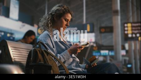 Woman Sits in International Airport Terminal, Using Smartphone Scan QR Code on Boarding Pass. Female Verifies Flight Data While Enjoying Cup of Coffee. Concept of Paperless Travel, Digital Check In. Stock Photo